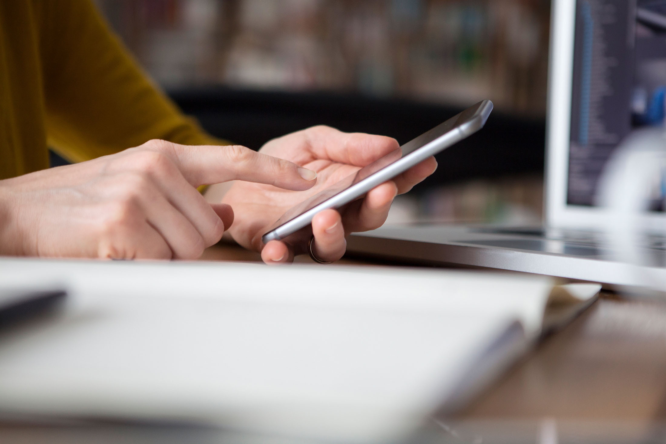 Weibliche Hände halten auf dem Schreibtisch ein Handy in der Hand