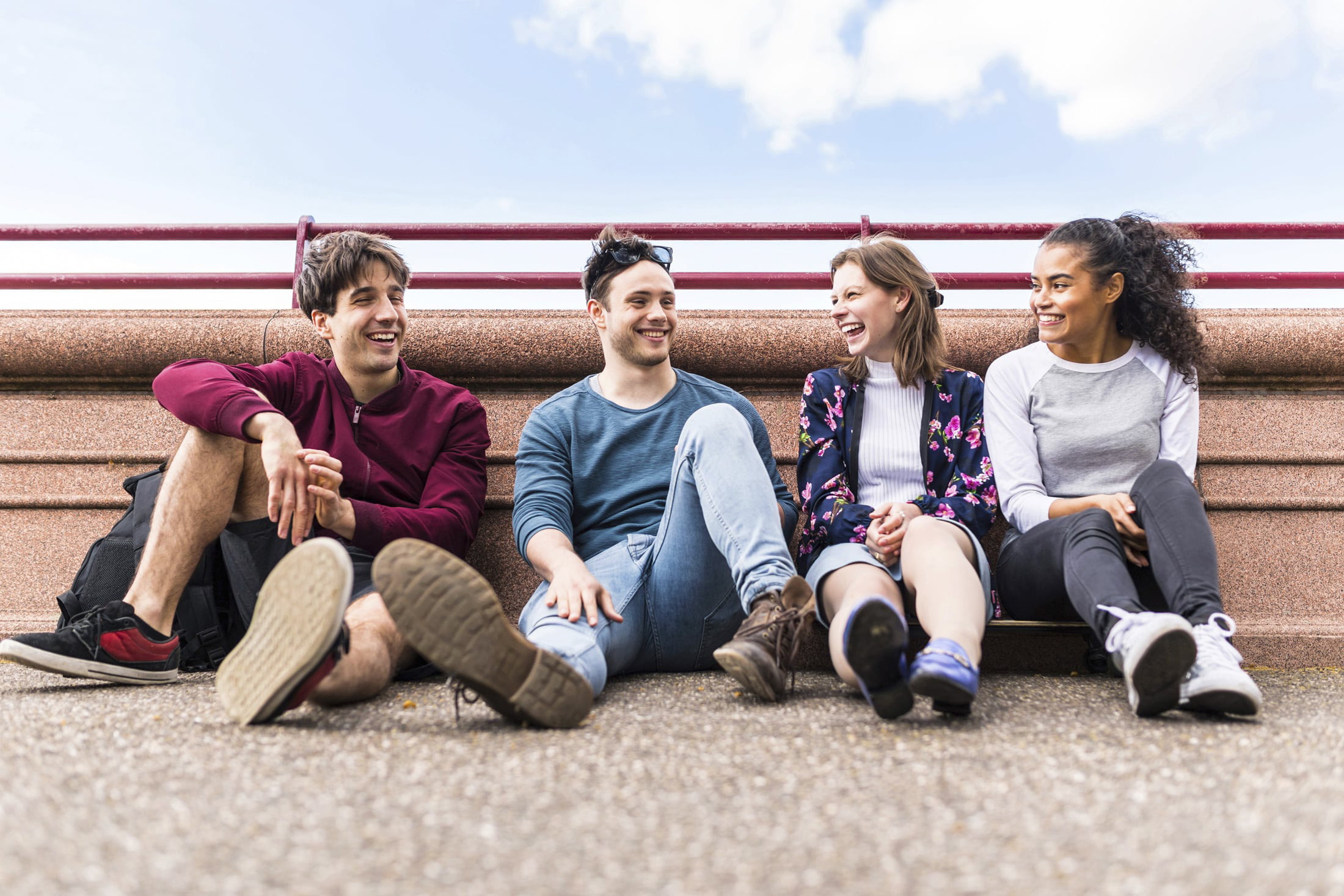 Vier junge Menschen sitzen an einem Geländer am Straßenrand