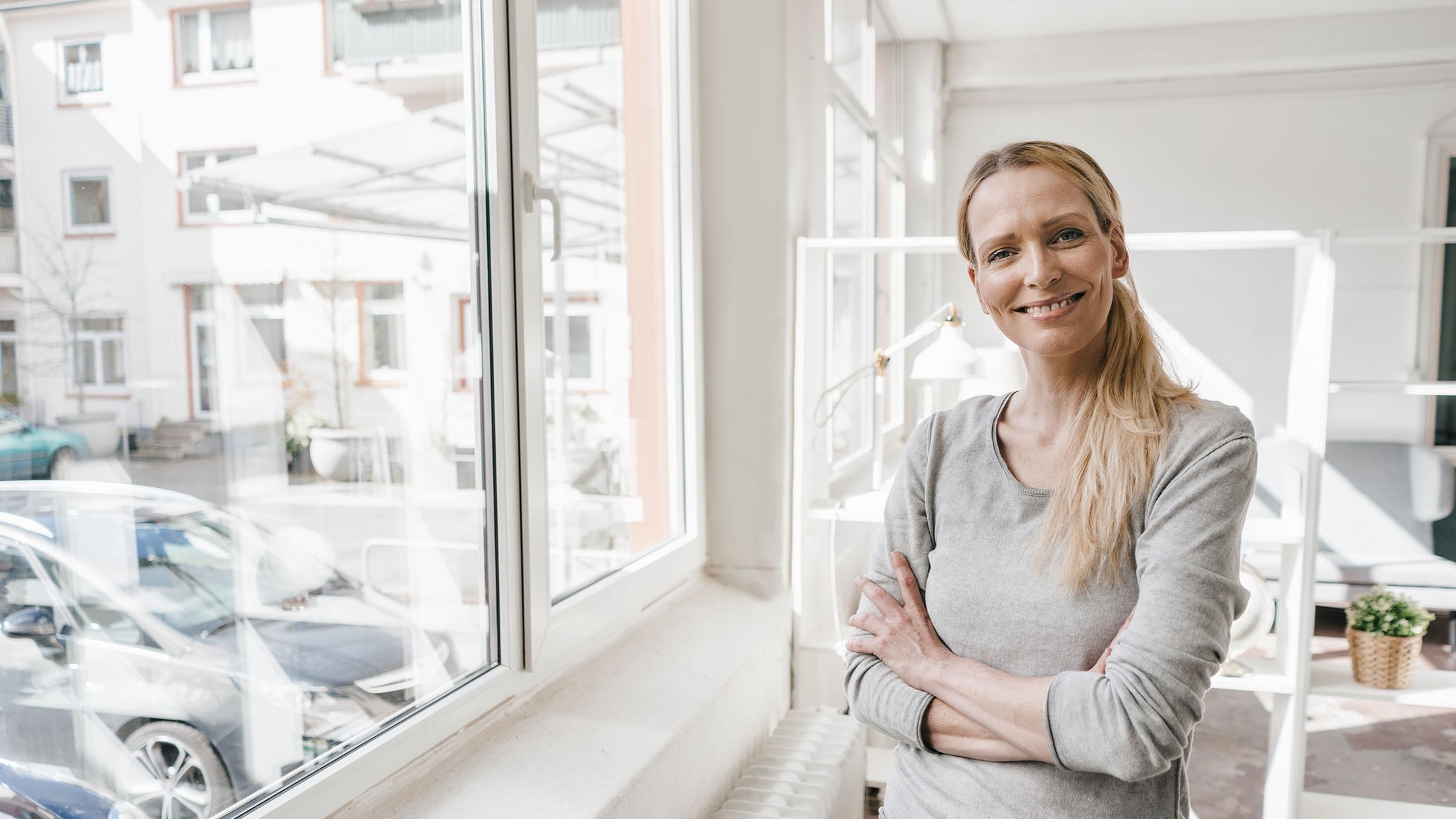 Portrait einer lächelnden Frau die vorm Fenster steht