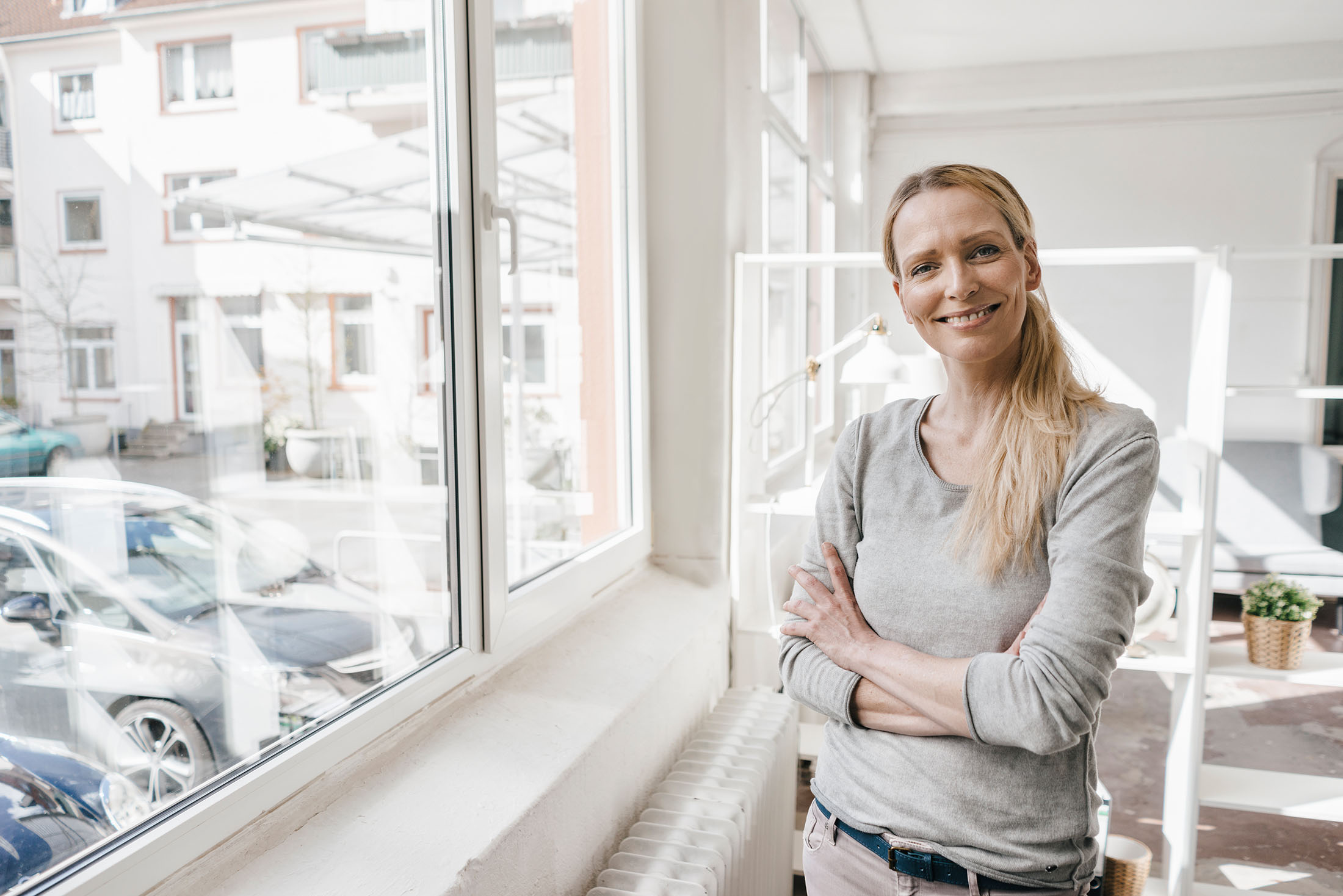 Portrait einer lächelnden Frau die vorm Fenster steht