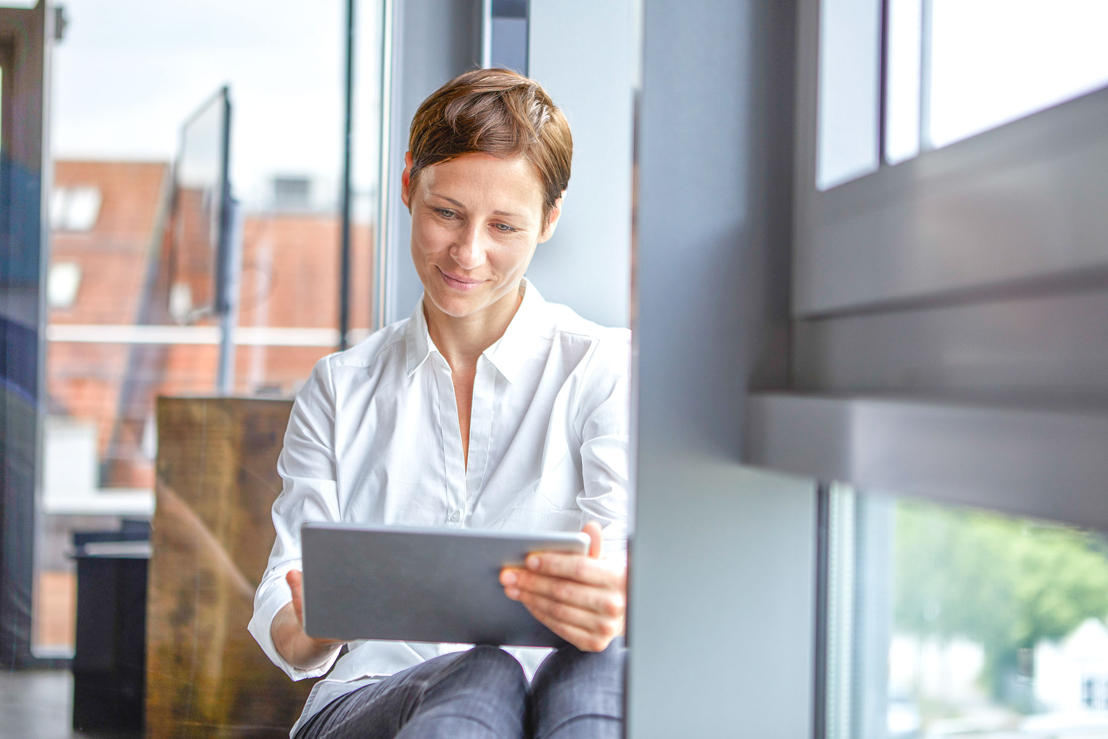 Geschäftsfrau sitzt im Büro am Fenster und nutzt ihr Tablet