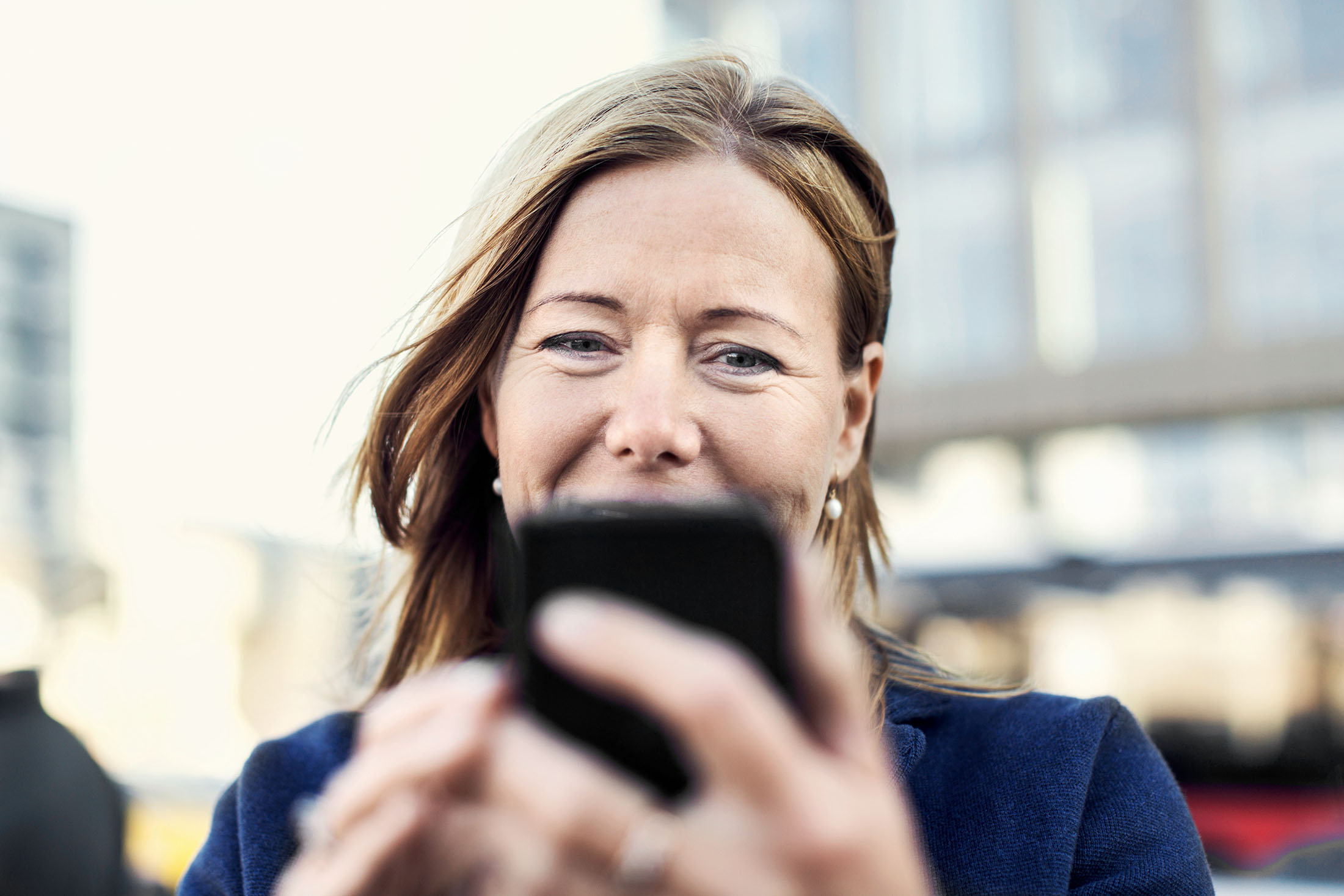 Geschäftsfrau steht auf der Straße und schaut lächelnd auf ihr Mobiltelefon