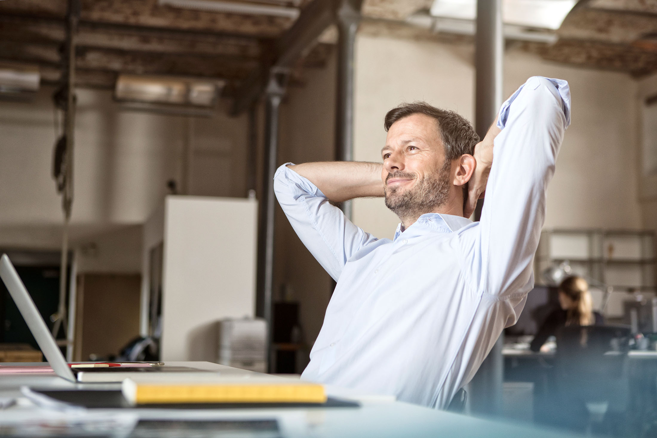 Mann sitzt im Büro am Schreibtisch, lehnt sich zurück und legt seine Hände hinter den Kopf