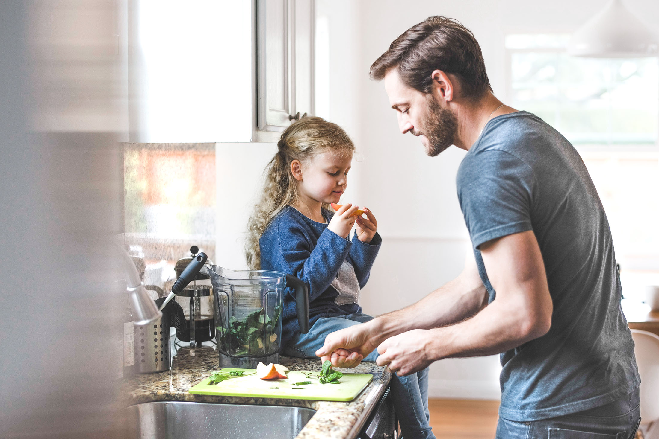 Seitenansicht von Vater und Tochter während der Vater kocht und die Tochter einen Apfel isst