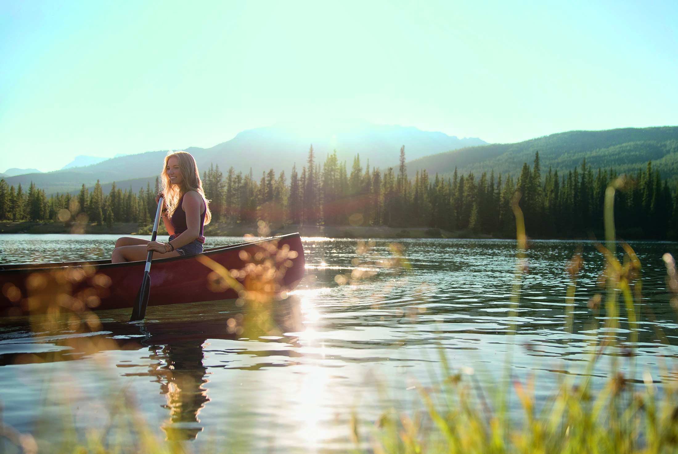Junge Frau paddelt ein Kanu auf einem von Wäldern umgebenen See
