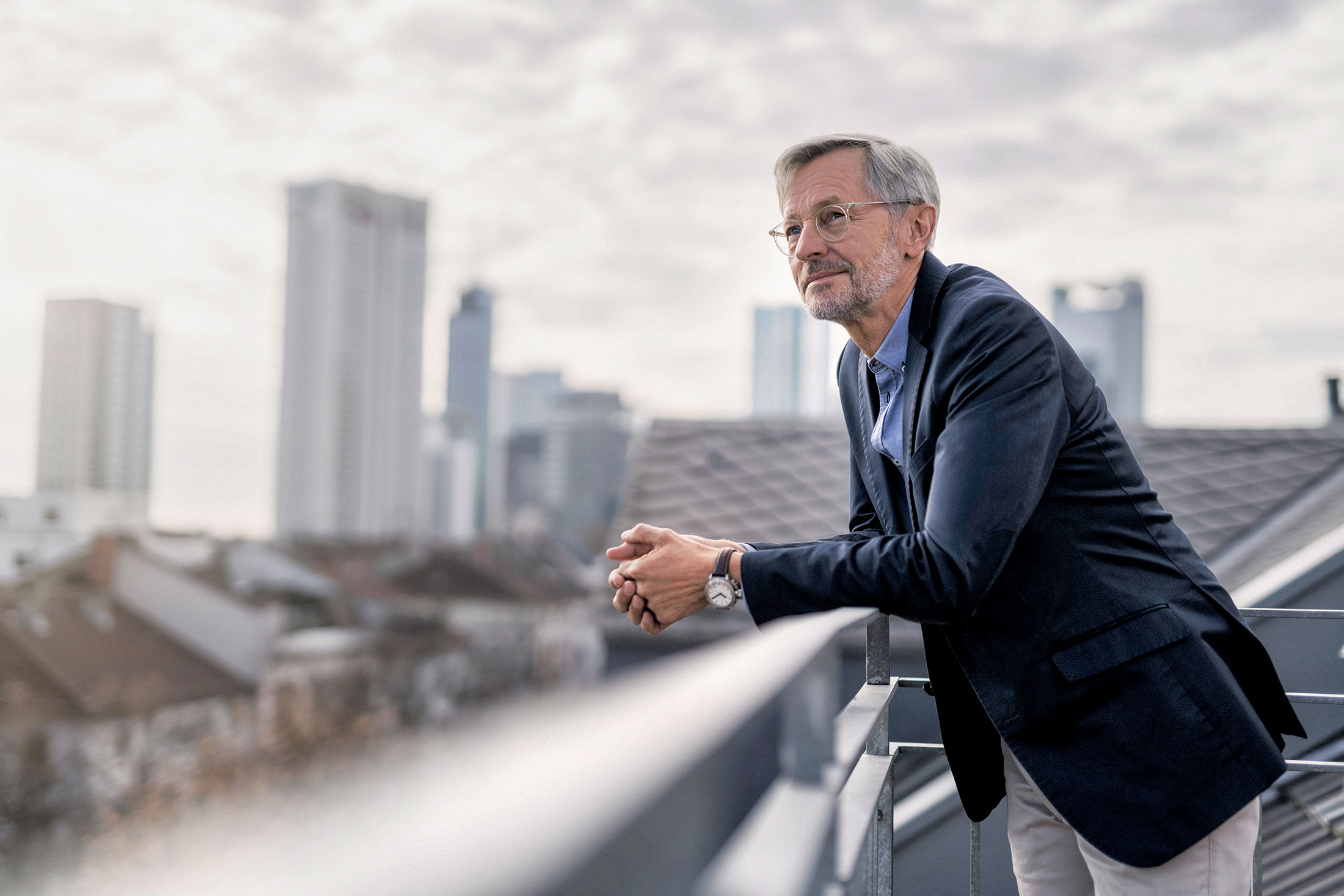 Älterer Geschäftsmann steht auf einem Balkon und schaut in die Ferne