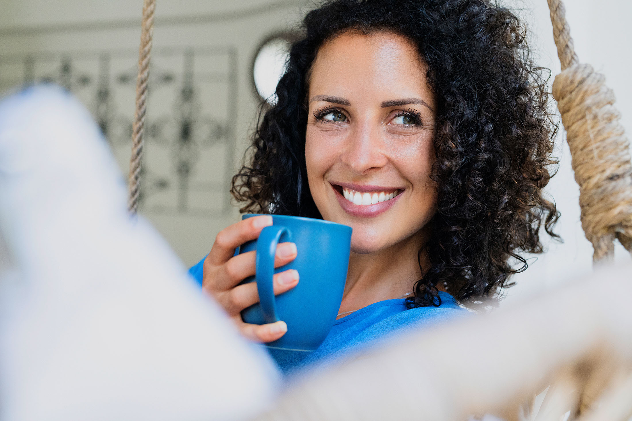 Lächelnde Frau mit Locken hält eine Tasse Kaffee