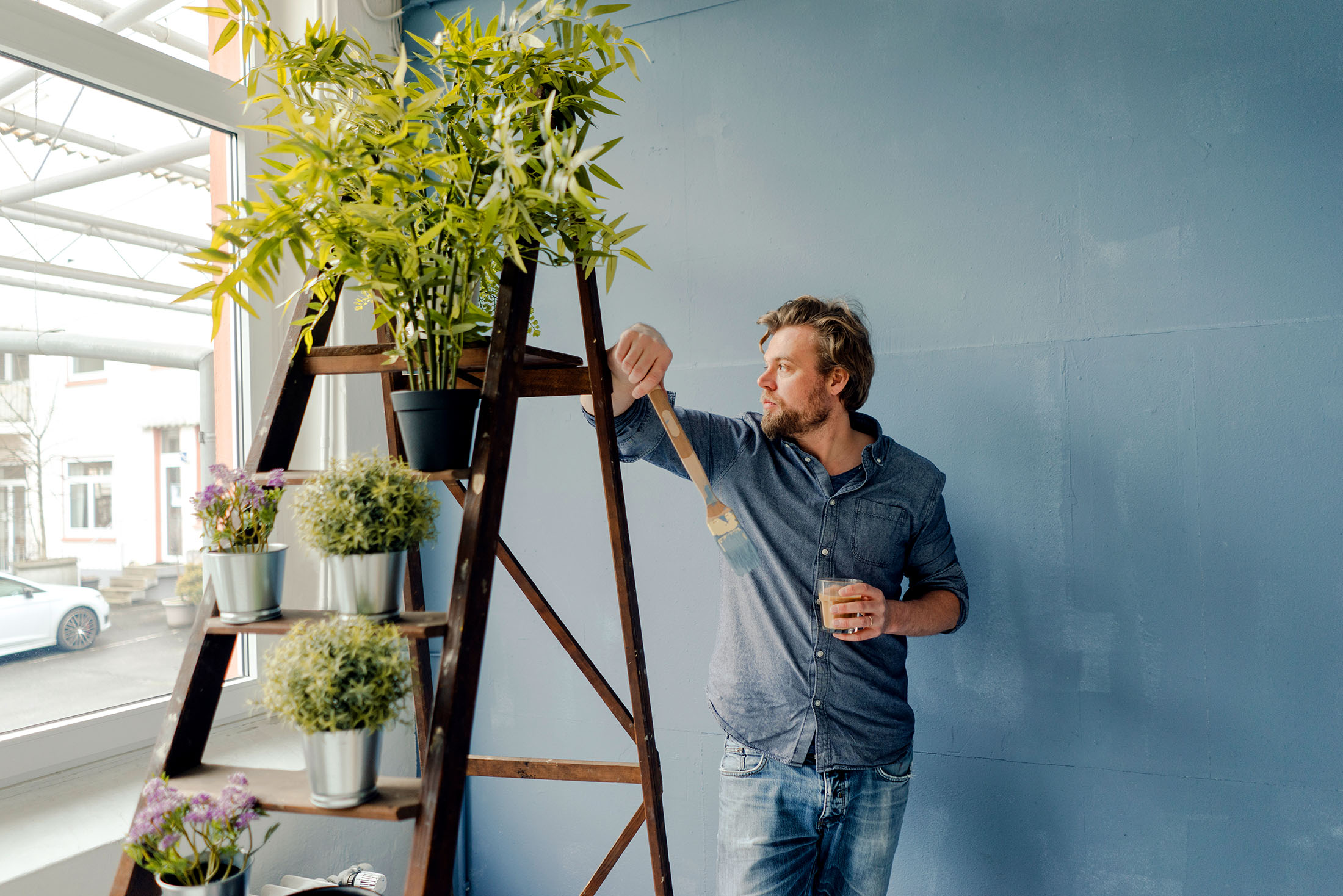 Mann mit Kaffeeglas und Pinsel in der Hand schaut aus dem Fenster