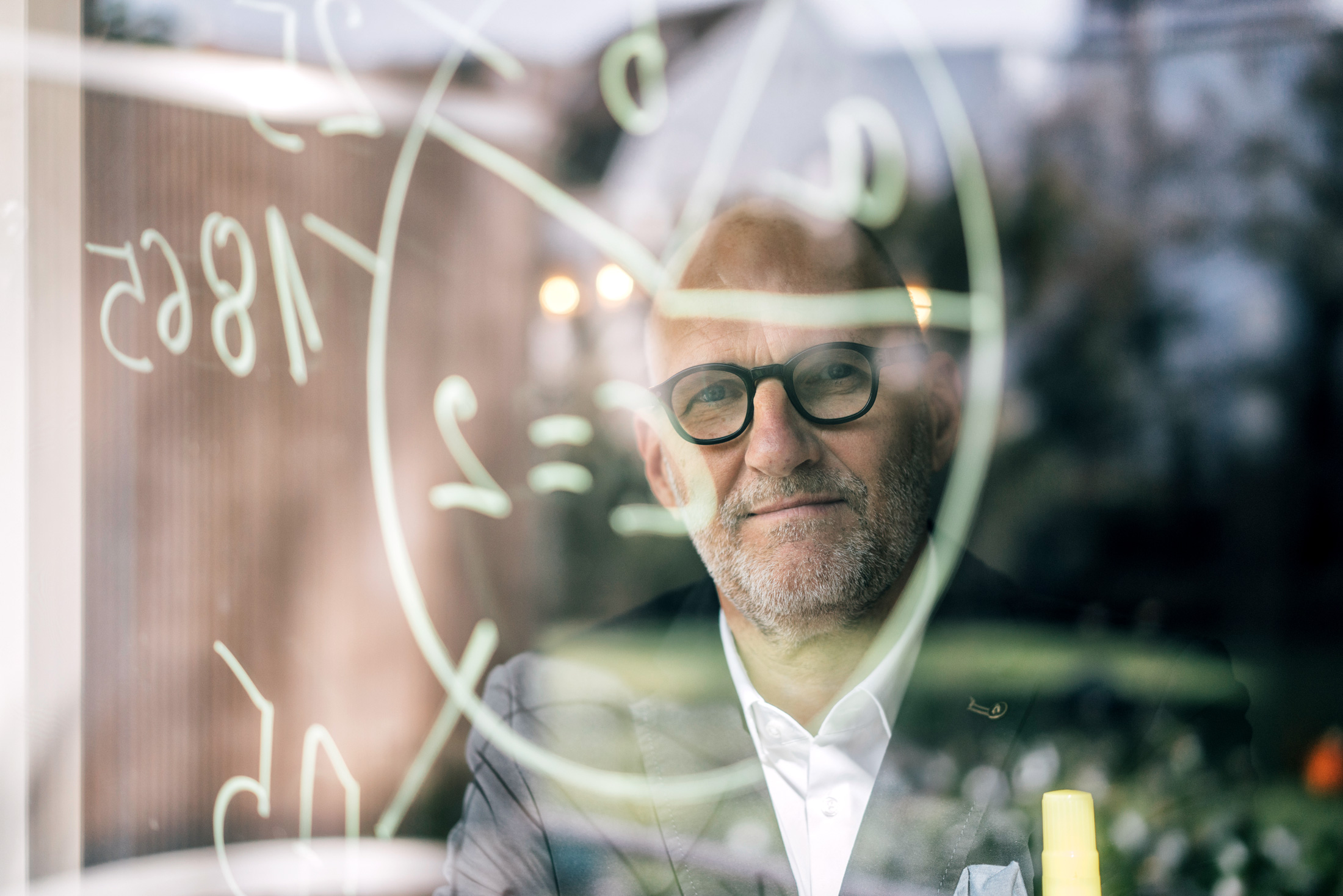 Älterer Geschäftsmann brainstorming, malt Formeln an ein durchsichtiges Board