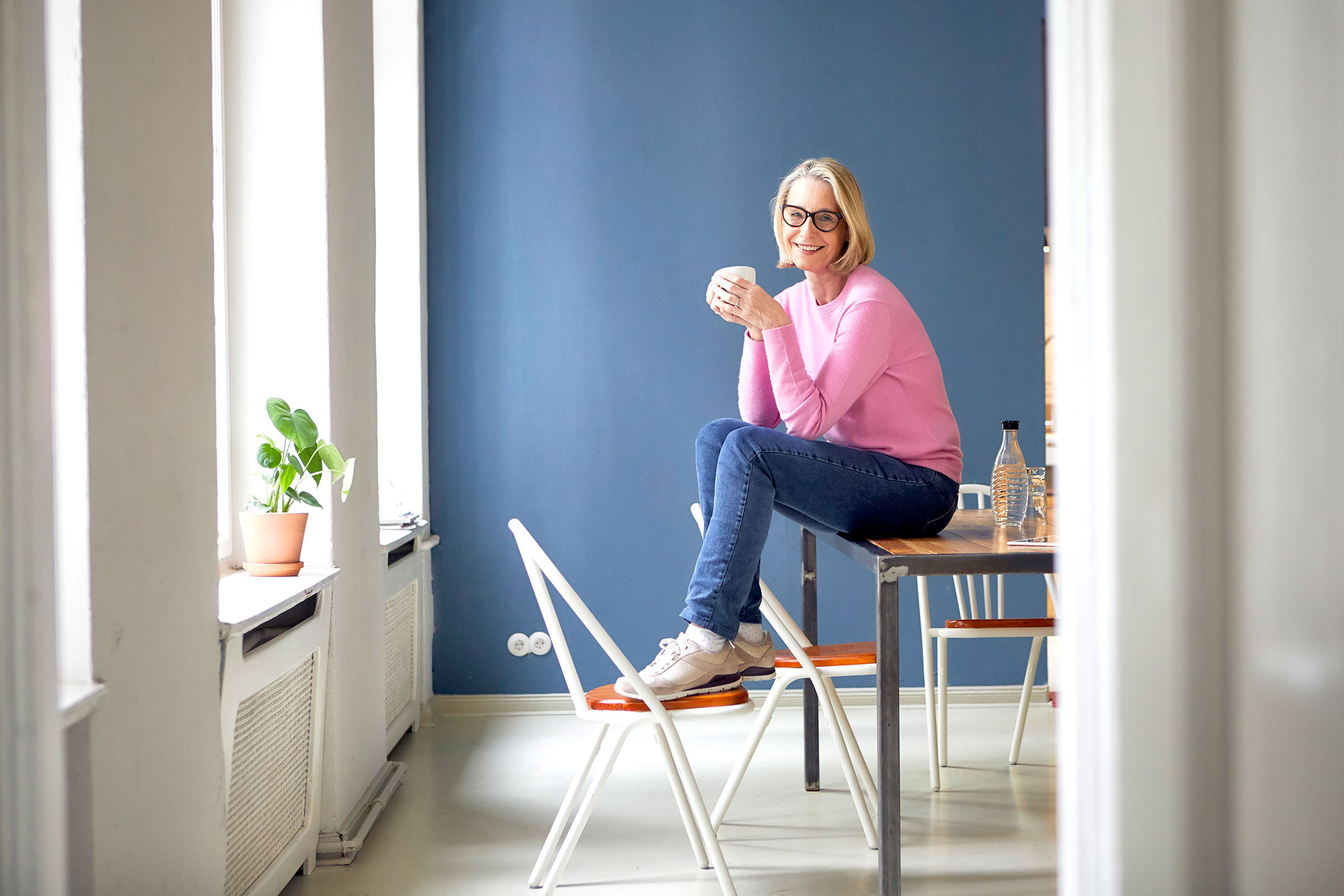 Frau mittleren Alters sitzt lächelnd mit einer Tasse auf einem Tisch