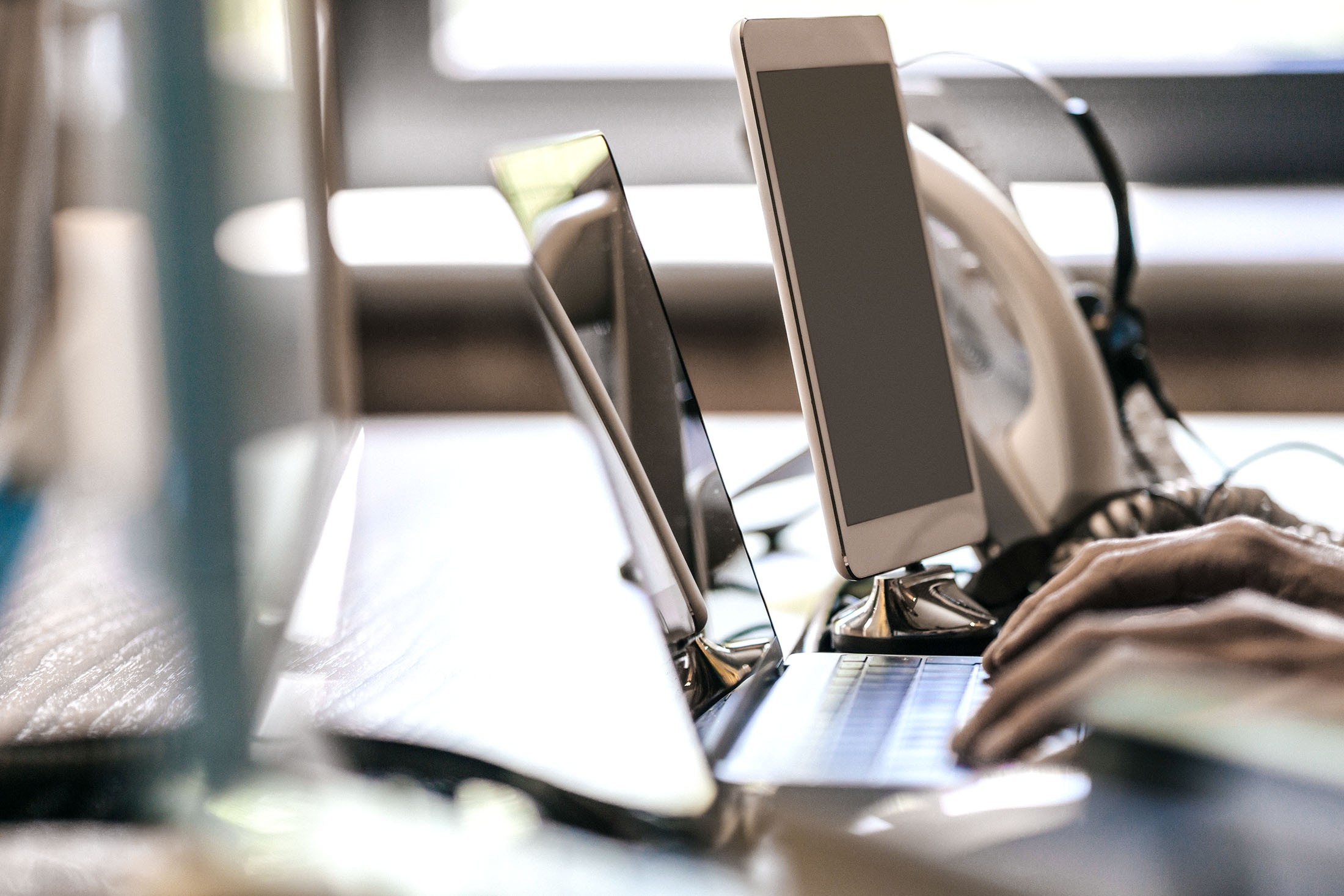 Hände arbeiten an einem Laptop am Schreibtisch mit Tablet Computer und Telefon im Hintergrund