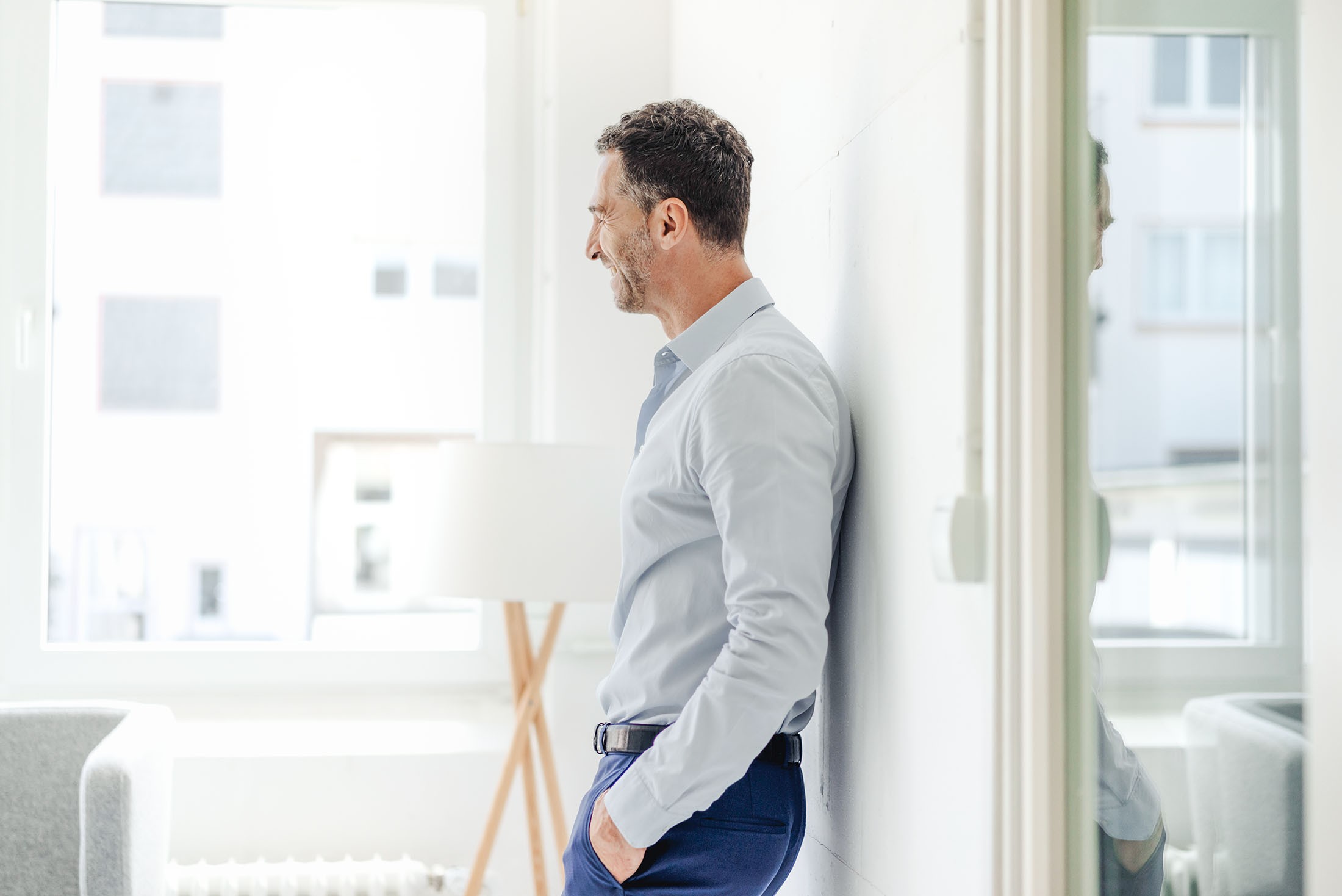 Lächelnder Geschäftsmann lehnt in seinem Büro an der Wand