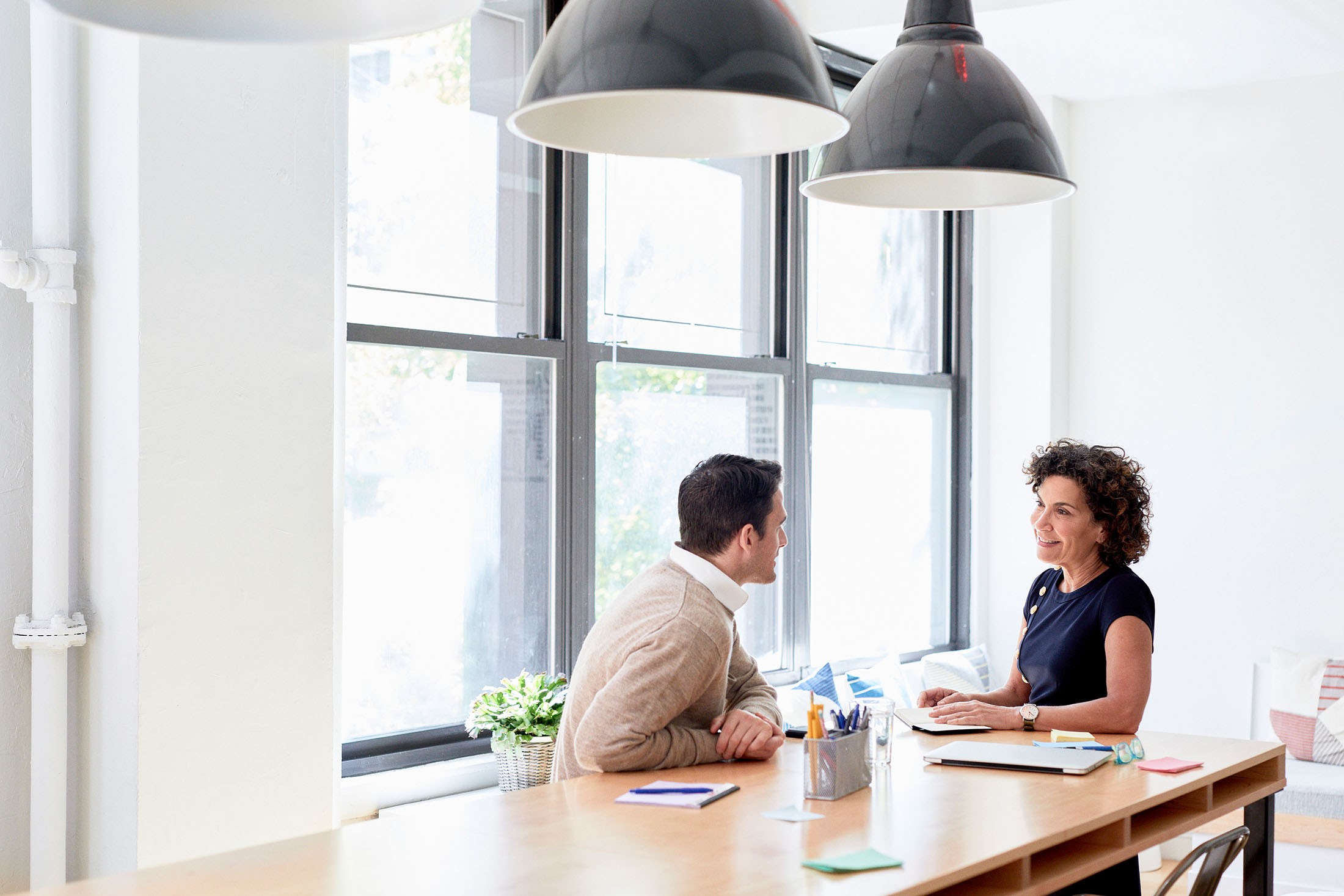 Arbeitskollegen diskutieren am Konferenztisch an Fenstern in einem kreativen Büro