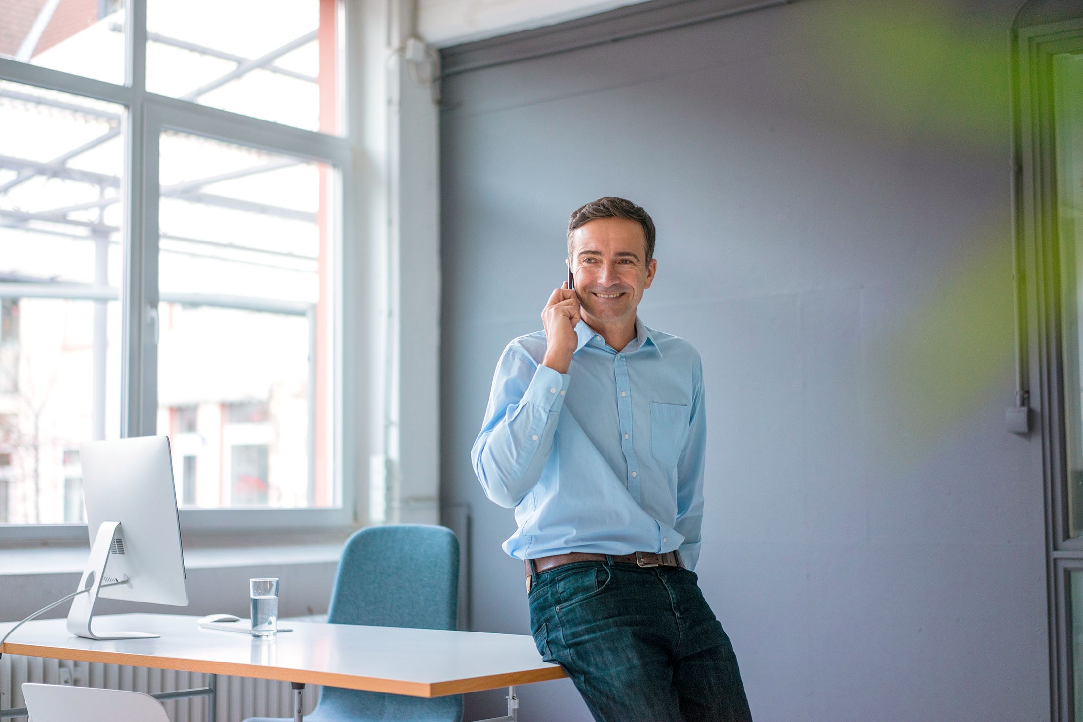 Lächelnder Geschäftsmann an seinem Telefon im Büro