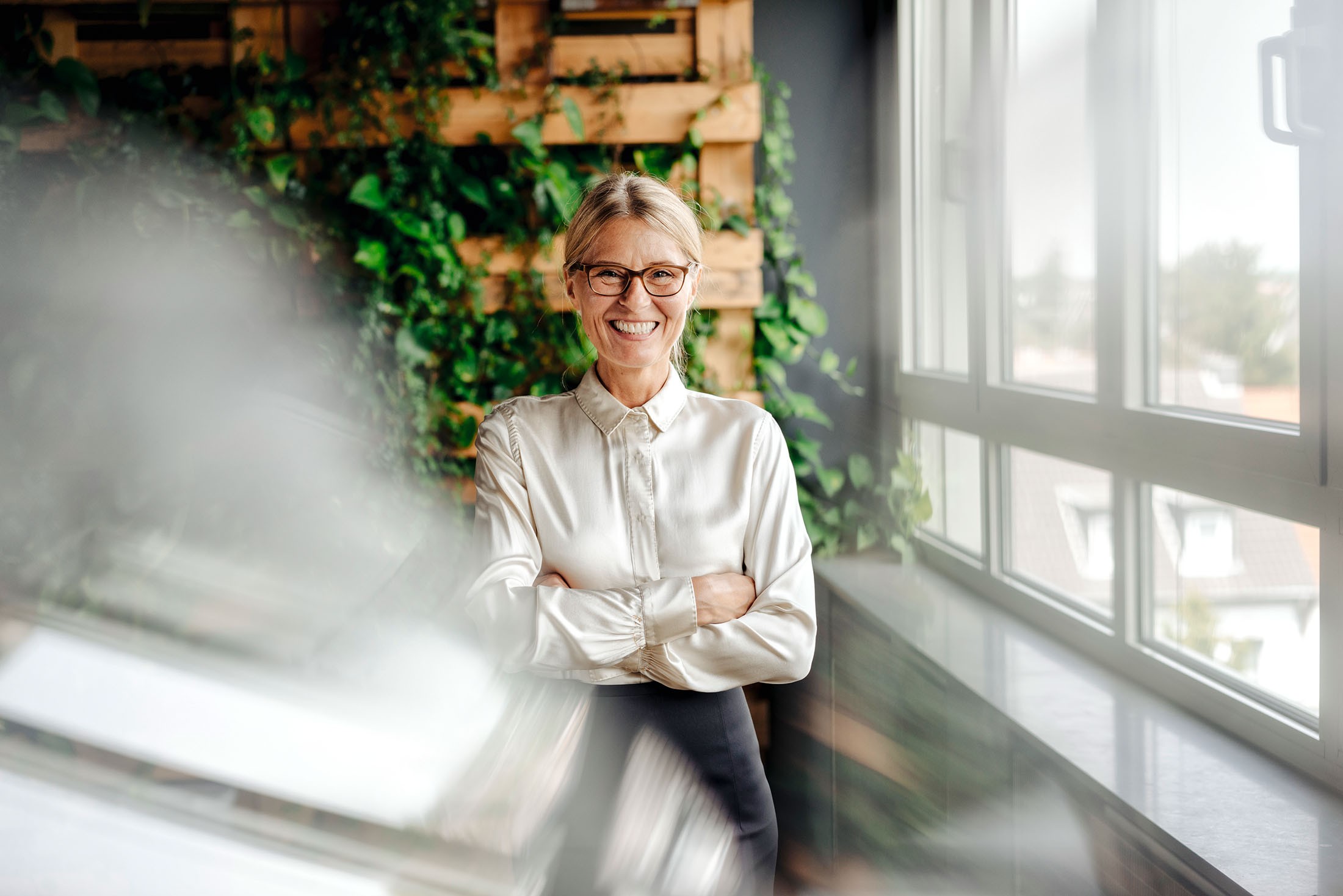 Portrait von einer glücklichen Geschäftsfrau in einem grünen Büro vorm Fenster