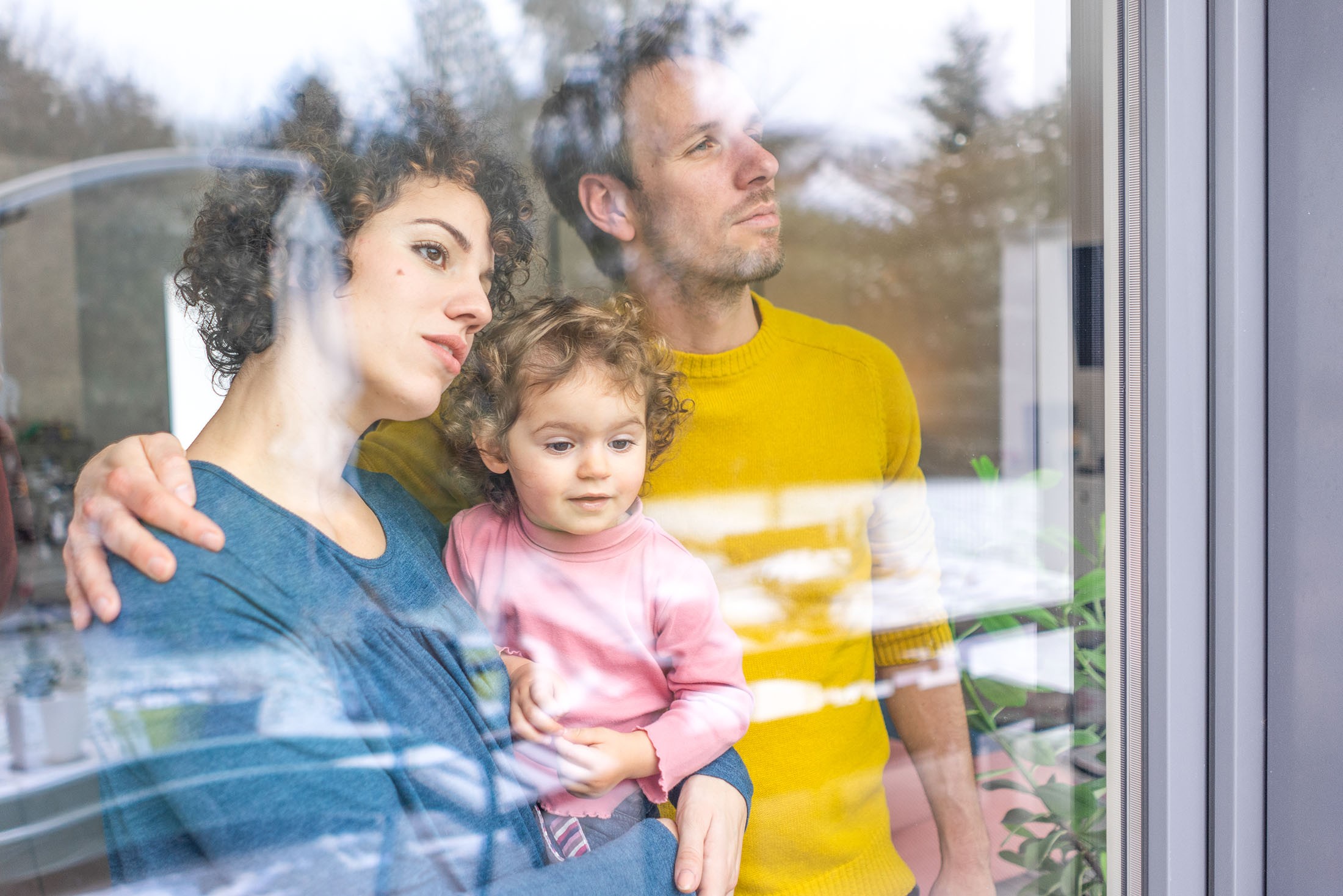 Familie schaut aus dem Fenster, Mutter hält Tochter