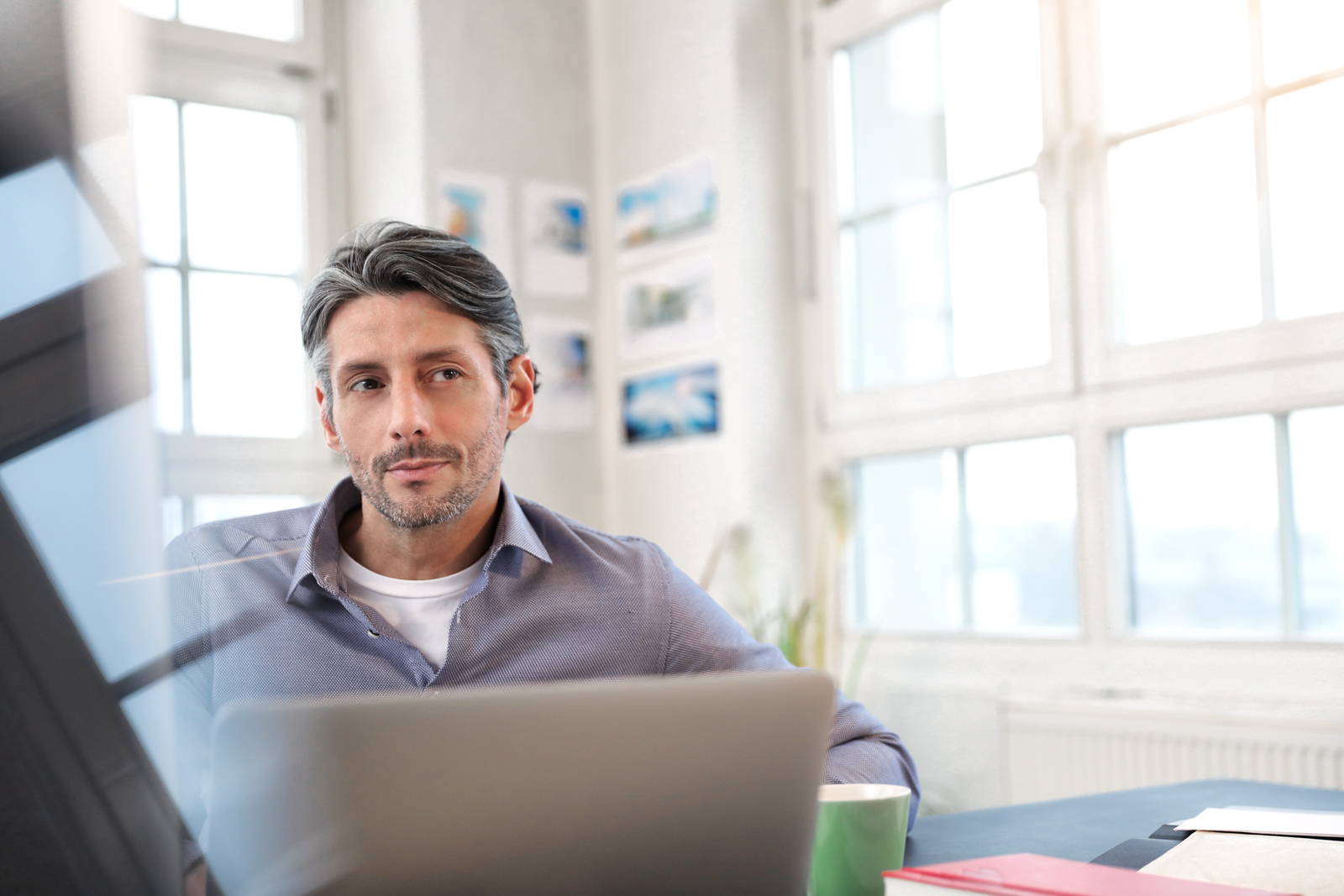 Mann sitzt am Laptop mit einer Tasse Kaffe und schaut nachdenklich