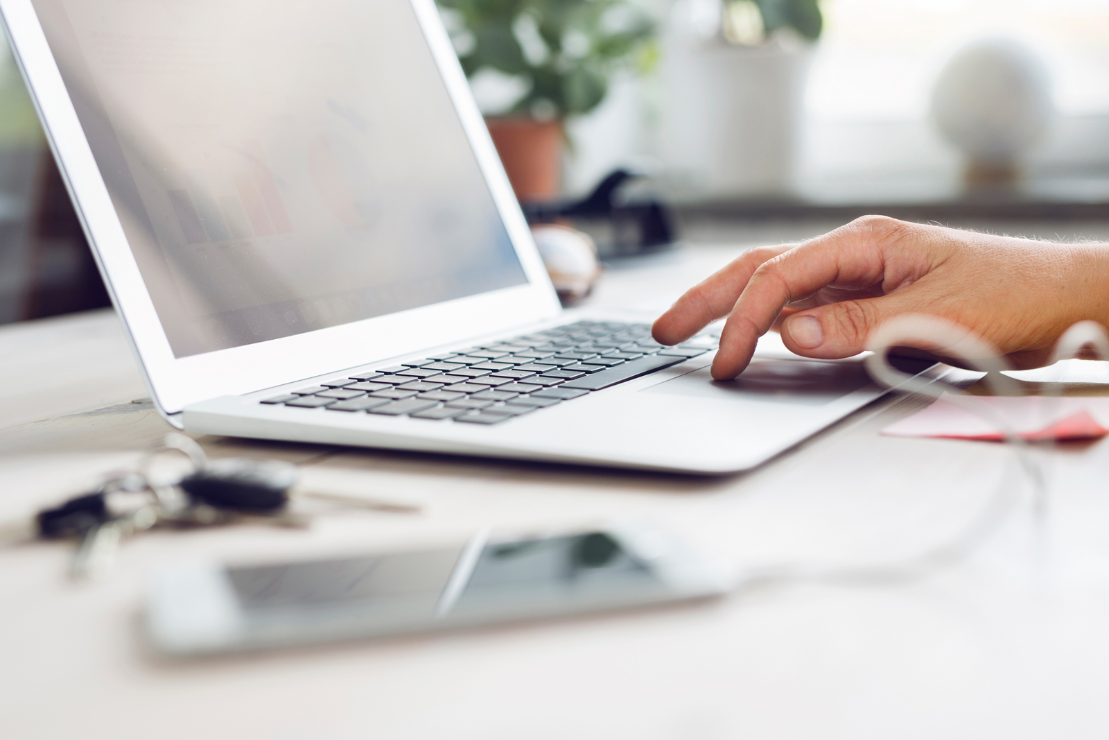 Hand arbeitet an einem Laptop, Schlüssel und Handy im Vordergrund