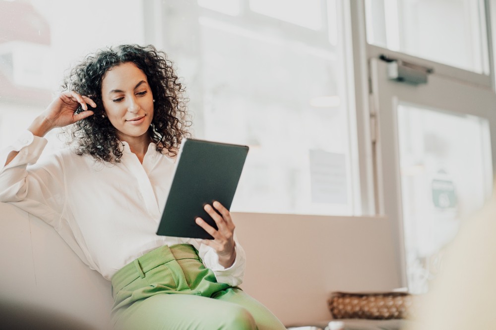 Junge Frau sitzt und schaut auf ein Tablet